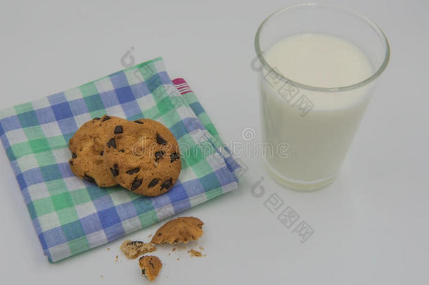 一块布上的巧克力片饼干和白色背景上的一杯牛奶。