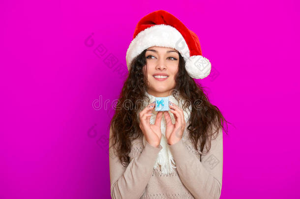 女孩在圣诞帽肖像与小礼品盒摆在粉红色背景，圣诞节假期的概念，快乐和情感