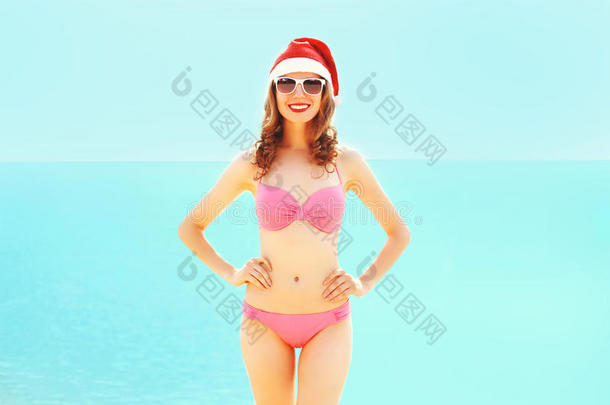 圣诞节漂亮的微笑女人戴着红色圣诞帽在海边海滩上