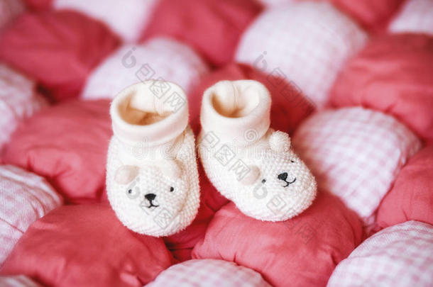 红色毯子上可爱的白色婴儿靴。 怀孕概念