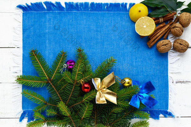 圣诞背景。 树枝云杉装饰着五颜六色的装饰品，坚果，肉桂，柠檬在蓝色餐巾纸上