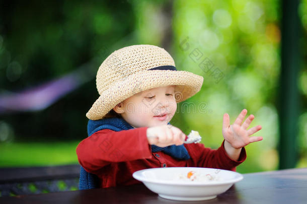 可爱的蹒跚学步的男孩在户外吃米饭麦片