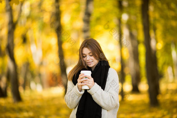 女孩在秋天的黄色阳光公园喝咖啡
