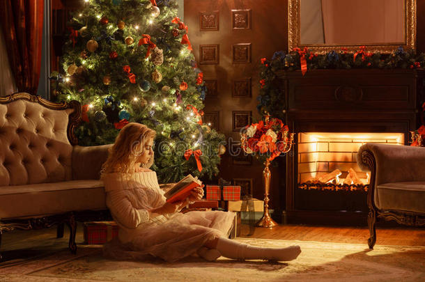 圣诞夜。年轻漂亮的金发女子在古典公寓的壁炉旁看书，装饰着圣诞树。
