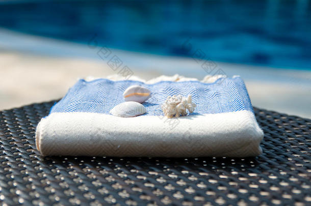 蓝色和白色土耳其毛巾的特写在藤椅上，蓝色游泳池为背景。