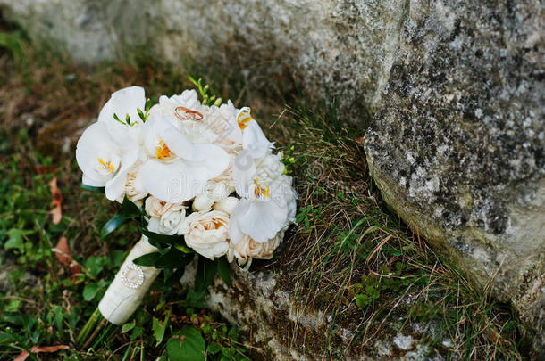 优雅的婚礼花束白色兰花，<strong>金色</strong>的结婚戒指在<strong>草地</strong>背景石上。