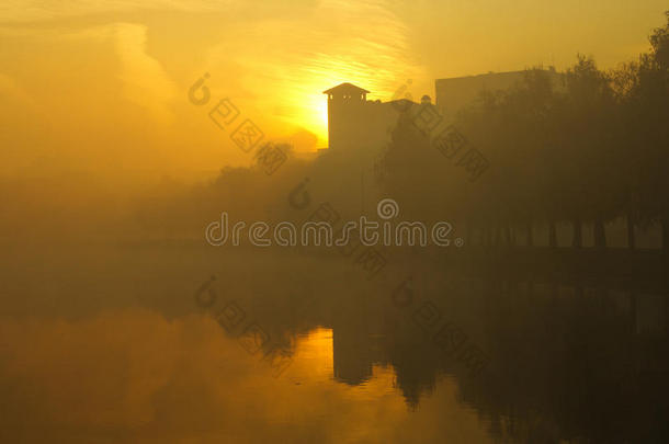 雾蒙蒙的早晨笼罩着湖面，秋天的树木倒映在水中