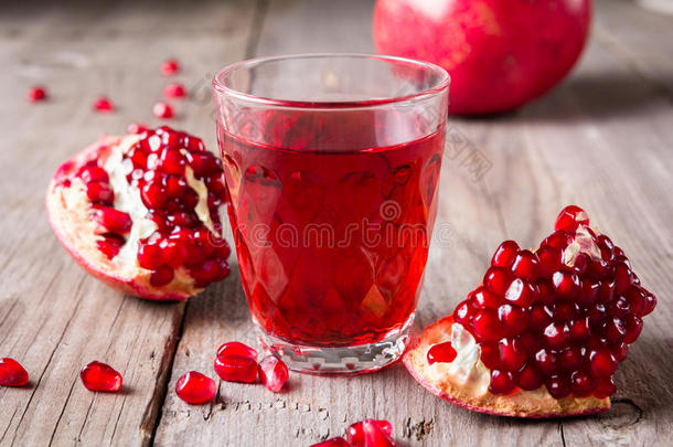 破碎的红色成熟多汁的石榴和一杯新鲜的果汁在乡村的木制未涂漆的桌子上