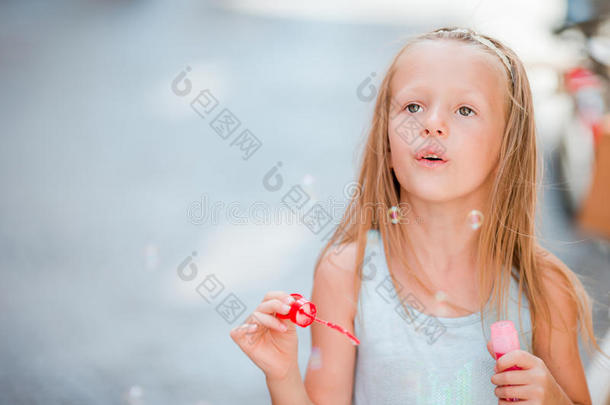 可爱的小女孩在户外吹肥皂泡在欧洲城市。 白种人孩子的肖像享受暑假