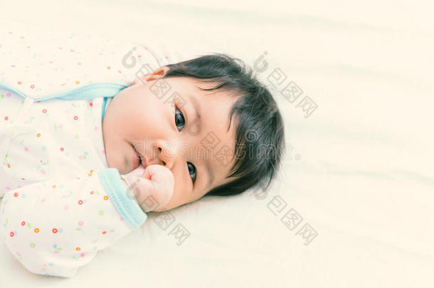 可爱的亚洲婴儿在床上吮吸。 （暖色调）
