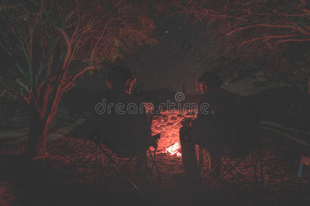 一对夫妇晚上坐在燃烧的篝火旁。 在非洲纳米比亚<strong>星空下</strong>的森林露营。 夏天的冒险和