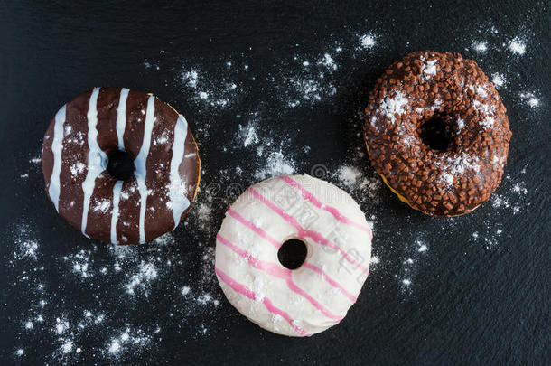 巧克力和釉面甜甜圈，粉红色，白色，黑色石头上的棕色，顶部视图