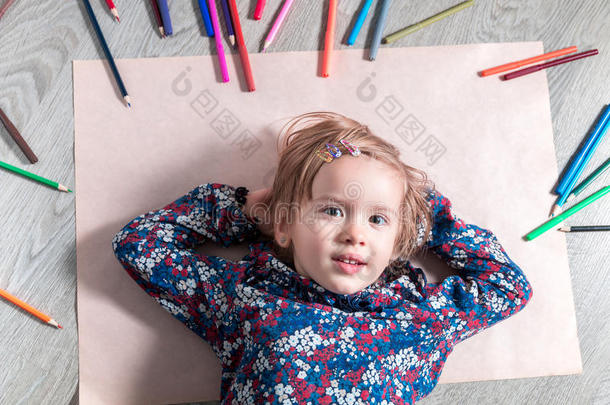 孩子躺在蜡笔附近的地板纸上。 小女孩画画。 上面的风景。 创造力的概念。