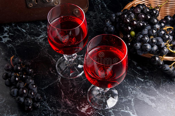 深色大理石背景上的一杯红酒。 背景上的一簇蓝色葡萄。。