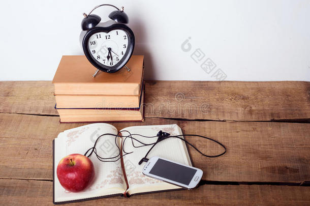 木制背景上的书籍、<strong>闹钟</strong>、记事本、<strong>手机</strong>和苹果