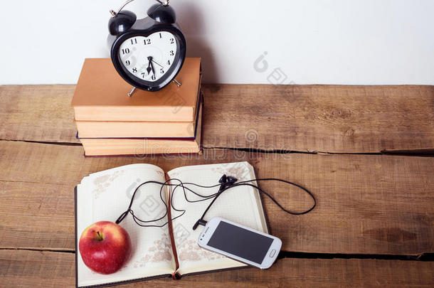 书籍，<strong>闹钟</strong>，记事本，带耳机的<strong>手机</strong>和木制背景上的苹果