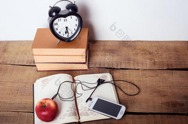书籍，闹钟，记事本，带耳机的手机和木制背景上的苹果