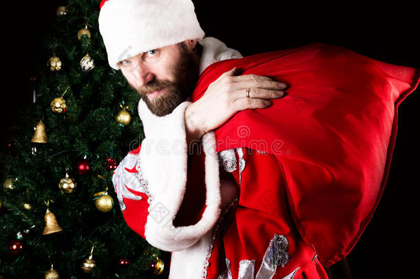坏残忍的圣诞老人背着一个袋子，在圣诞树的背景上恶意地微笑