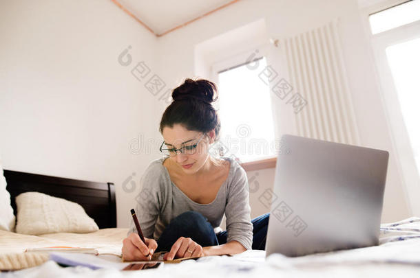 漂亮的年轻女人坐在床上工作。 家庭办公室。