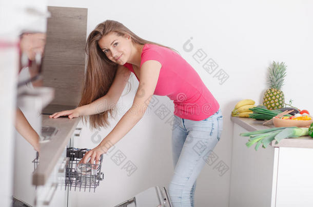 漂亮的年轻女人在洗碗机里做盘子。