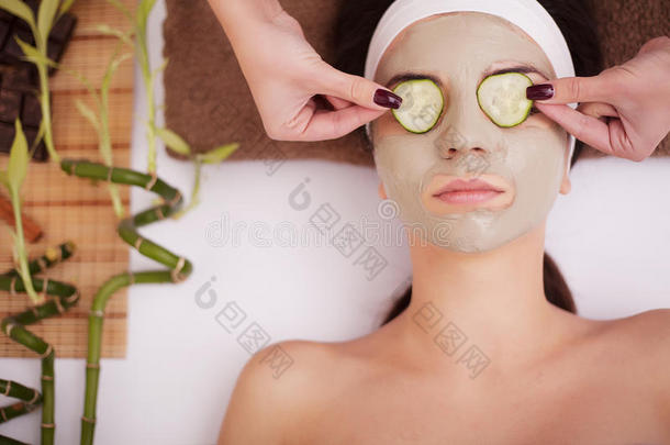 美丽的年轻女人戴着粘土泥面具，脸上覆盖着黄瓜片。