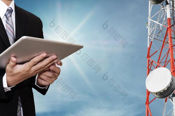 商人数字平板电脑上工作的商人，在蓝天上的电信塔上用卫星碟电信网络和阳光
