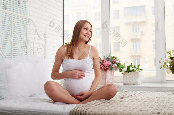 梦幻般的怀孕妈妈微笑着，坐在床上看着窗户