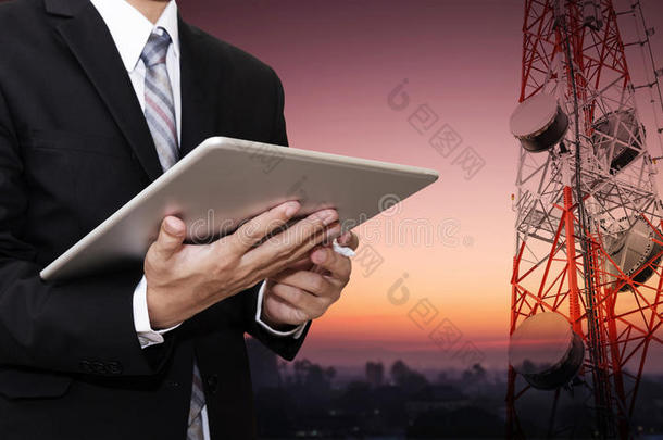 商人在数字平板电脑上工作，在农村城市的电信塔上有卫星天线电信网络