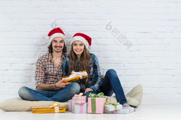 圣诞<strong>佳节</strong>快乐情侣坐在地板上戴着新年圣诞老人帽，男人和女人微笑着拿着礼物盒