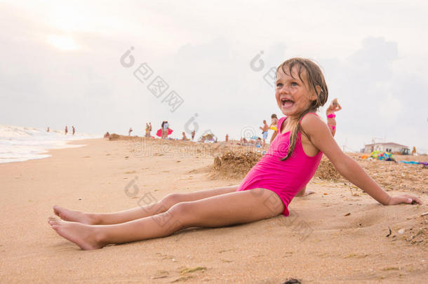 五岁的女孩坐在海滩上，在傍晚的海边，在阴天