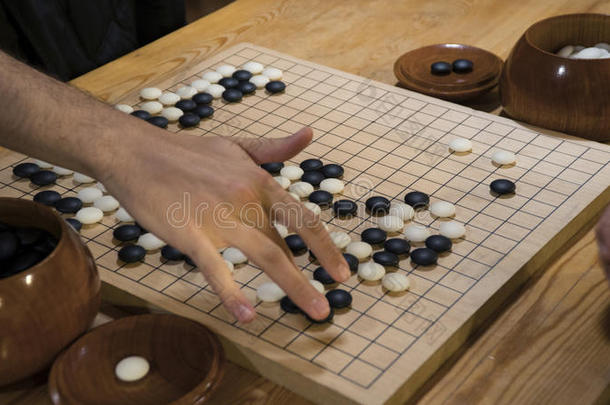 手在中国围棋或围棋游戏板上玩黑白。 室内活动与人工光。