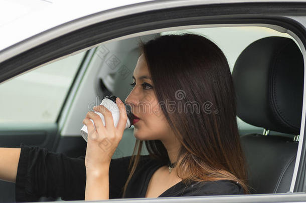 特写年轻女子坐在车里拿着咖啡杯喝酒，从外面的司机窗口看到，女司机