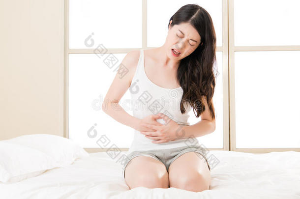 美丽的亚洲女人在床上胃痛