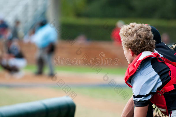 棒球捕手靠在挖出的栅栏上看着相机。