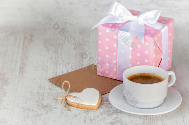 礼盒包裹着粉红色的虚线纸，心形的爱情饼干，一杯咖啡和一张白色木头上的空手道卡