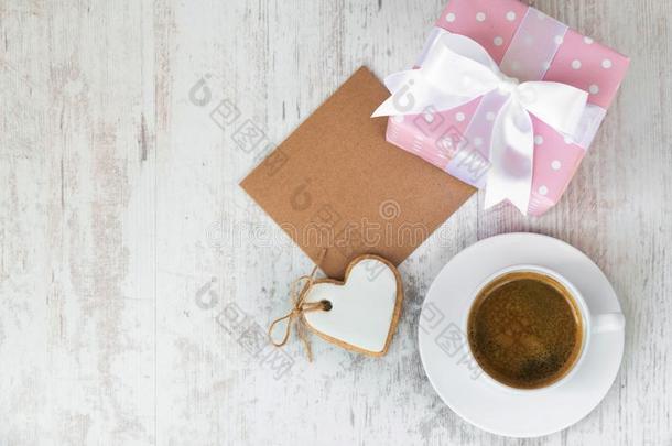 礼盒包裹着粉红色的虚线纸，心形的爱情饼干，一杯咖啡和一张白色木头上的空手道卡