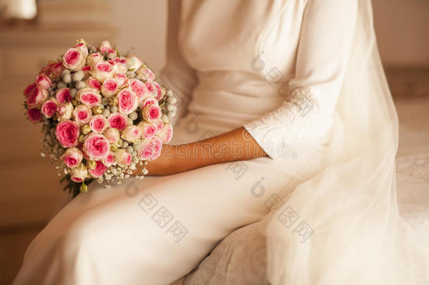 新娘坐在床上，拿着花束在白色的房间里