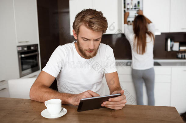 英俊的男人看着平板电脑。 女朋友厨房背景。