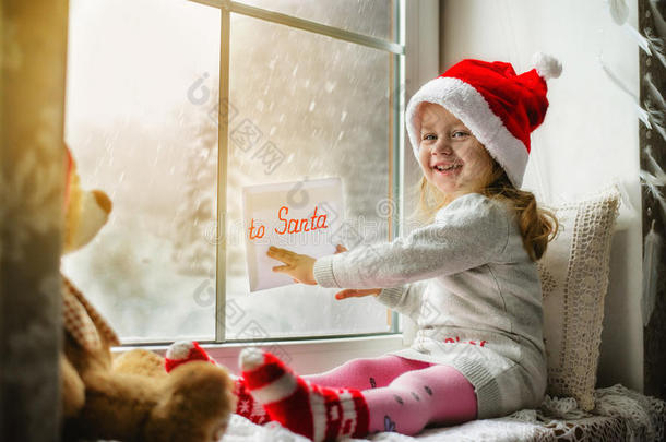 可爱的小女孩坐在窗边，给圣诞老人写了一封信