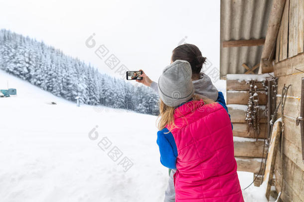 一对夫妇在智能手机上自拍照片，雪村木屋，男人，女人，冬天的雪