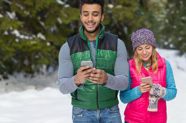 一对夫妇使用智能手机聊天在线雪林快乐微笑的男人和女人走在户外冬天
