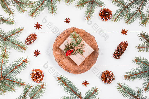 圣诞礼物在白色木制背景上的树桩上，有冷杉树枝、松果、红色装饰品