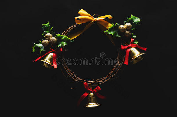 圣诞装饰，花环是从藤蔓的树枝上编织出来的，上面有金色的铃铛和绿叶，背景是黑色的，低调的
