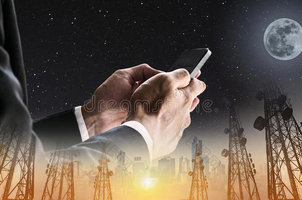 商人使用手机与双曝光全景电信塔和城市景观在日出和夜空