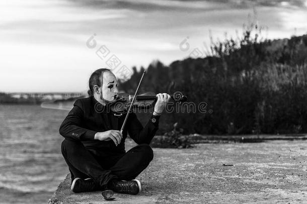 黑白照片，一个哑剧坐在<strong>河边</strong>，在户外拉<strong>小</strong>提琴
