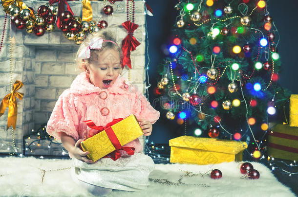 可爱的小女孩在装饰圣诞树附近收到一份礼物。