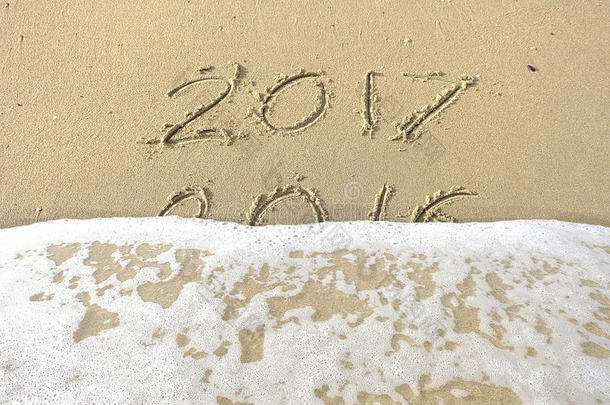 再见，2016你好，2017。铭文写在海滩沙滩上。