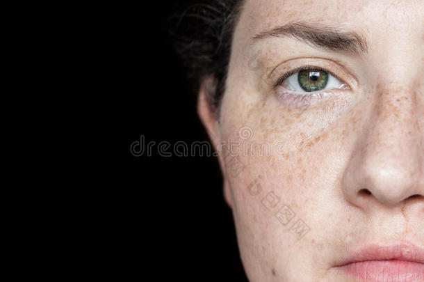 特写照片的女人有雀斑和绿色的眼睛孤立在一个黑色的背景：一半的脸可见在右侧的框架