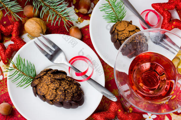 圣诞甜点巧克力锥在假日桌子上，葡萄酒，坚果和松树枝在红桌子上
