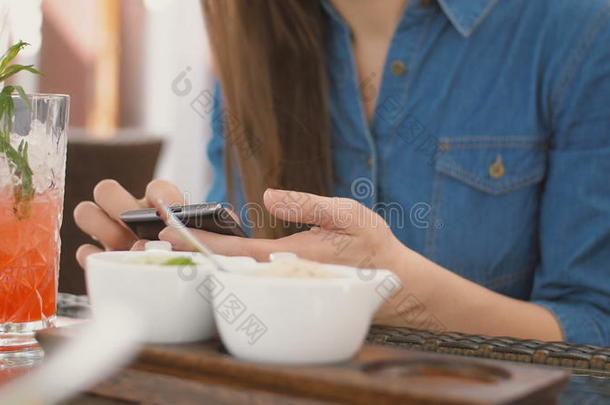 黑发女孩在咖啡馆里坐在外面用智能手机，用吸管喝一杯冷饮。 4k，